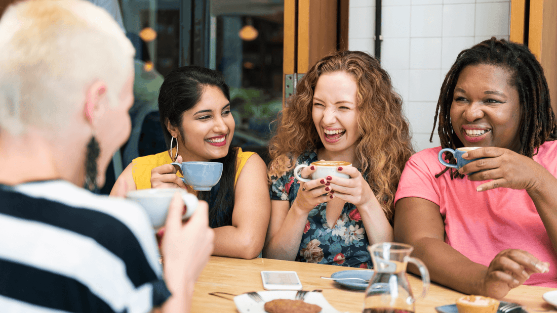 Four women of different ethnic backgrounds sit and laugh over coffee